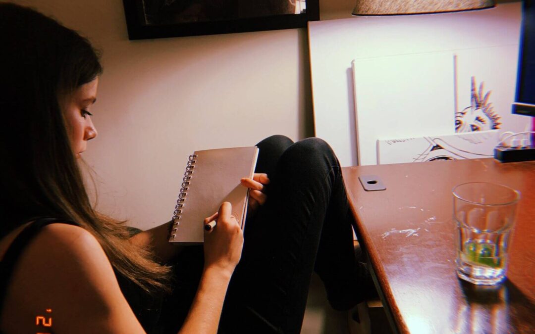 picture of a girl sitting at a desk drawing in a sketchbook