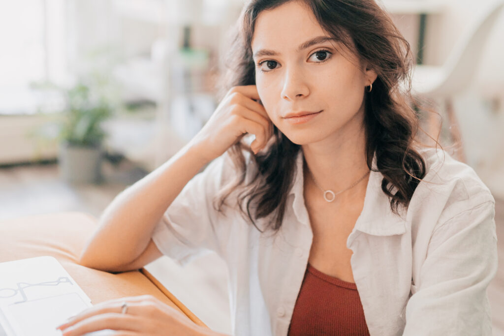 Young woman looking at camera, working at laptop on content marketing blog pieces.