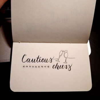 Micron pen. picture showing a card that says "cautious cheers" in a calligraphy font with two champagne glasses