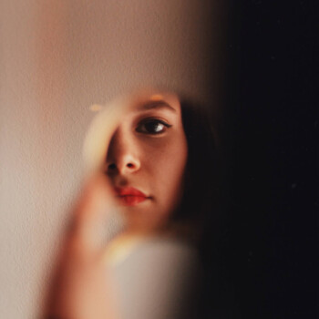 Photo by https://byabduls.com/work picture of a girl holding a compact mirror wearing red lipstick and black eyeliner
